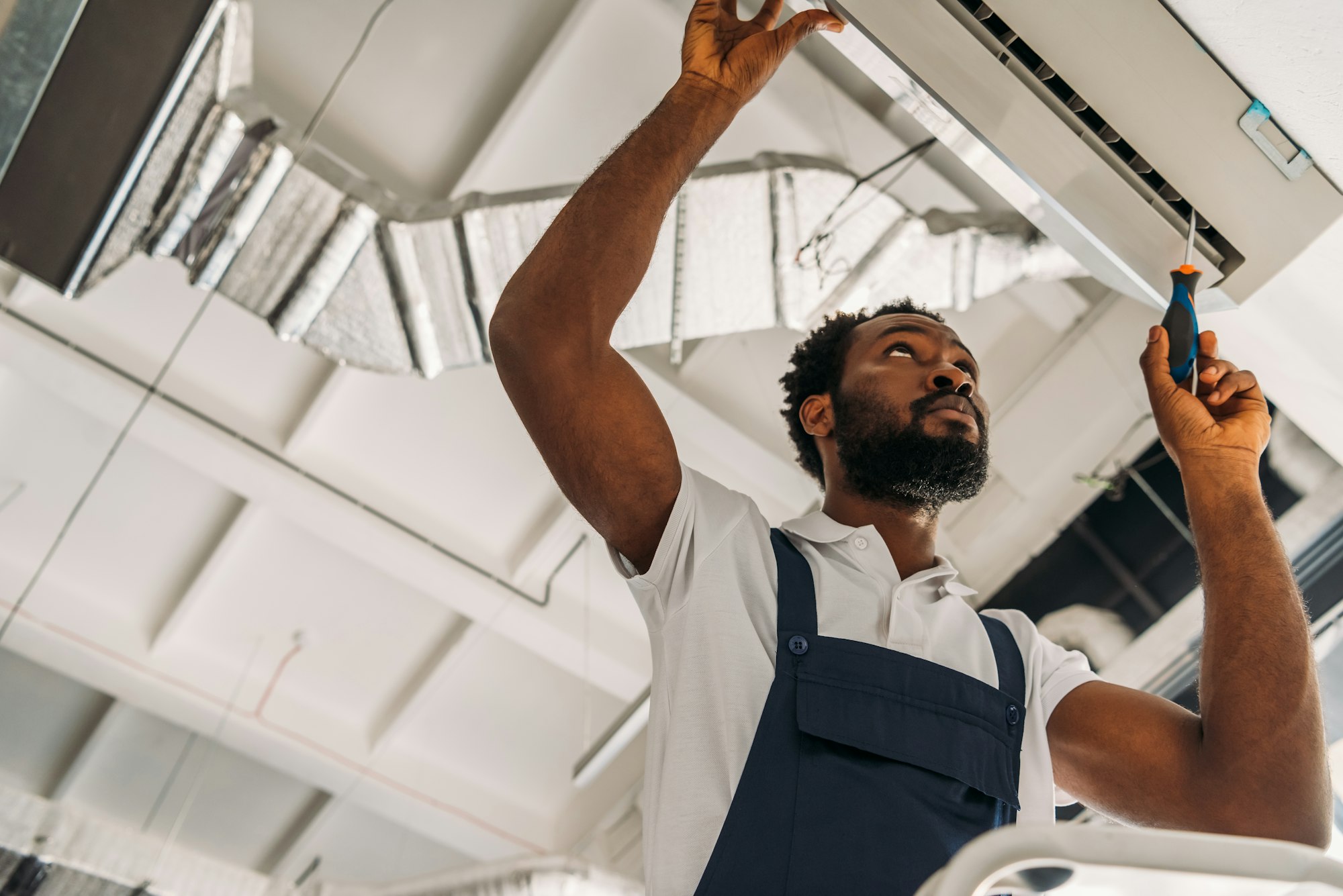 low-angle-view-of-african-american-handyman-repairing-air-conditioner-with-screwdriver